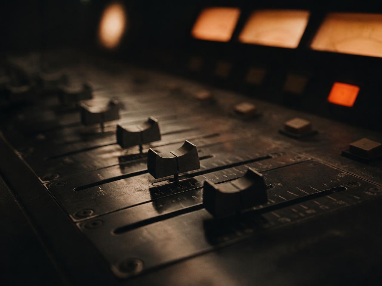 Faders on an analogue mixing desk in a dimly lit studio